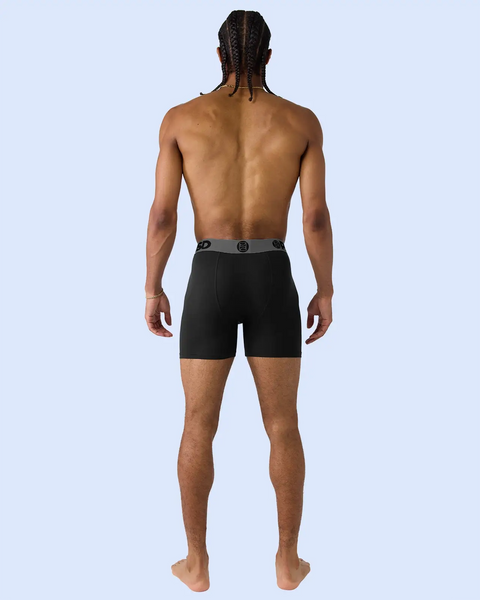 Man wearing black boxer shorts with logo waistband, shown from back view.